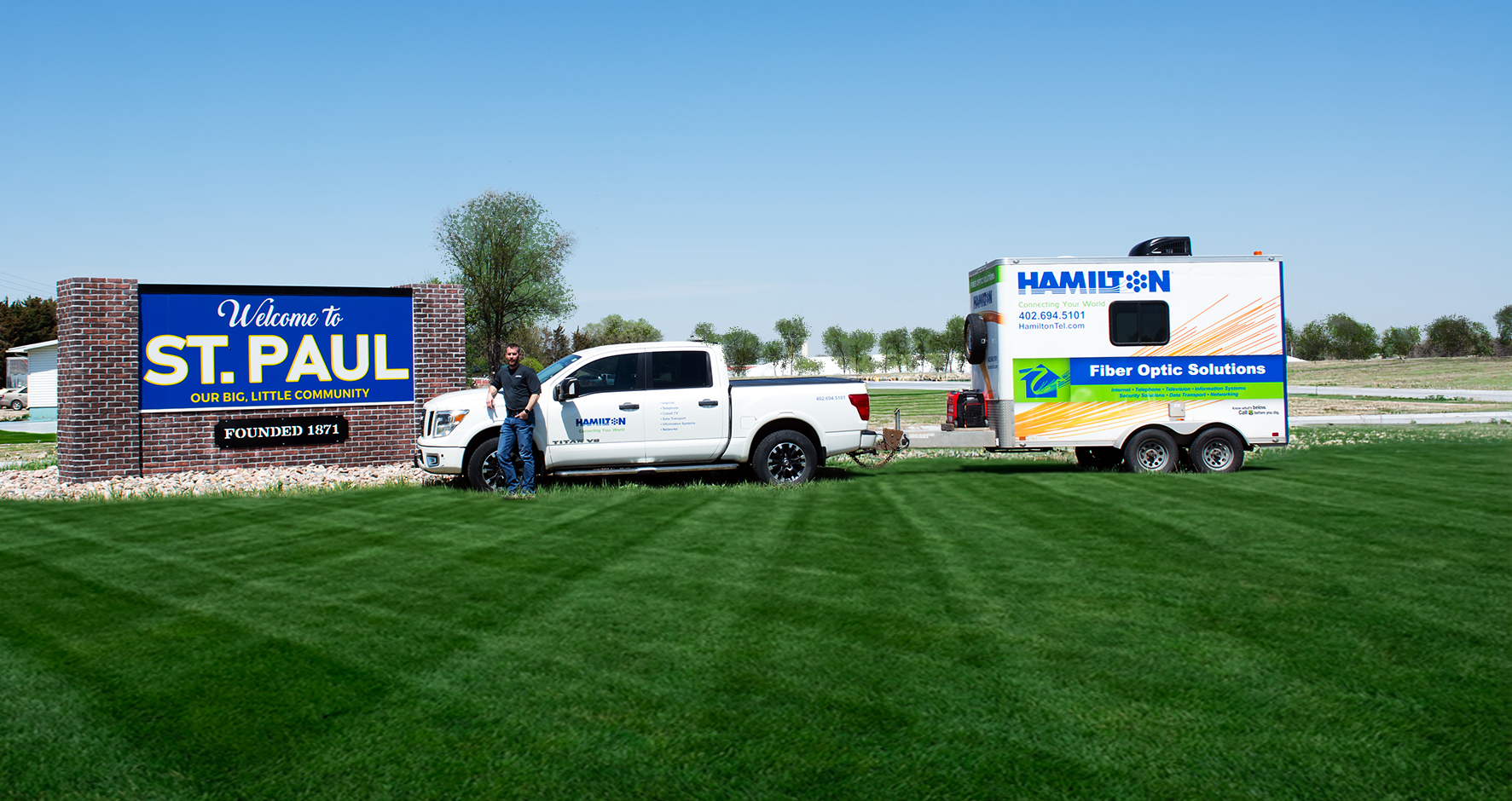 Hamilton fiber tech standing next to a hamilton fiber truck and trailer next to the St. Paul Nebraska city sign.
