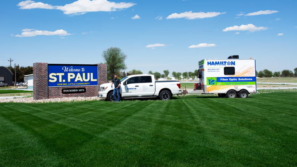 Hamilton fiber tech standing next to a hamilton fiber truck and trailer next to the St. Paul Nebraska city sign.